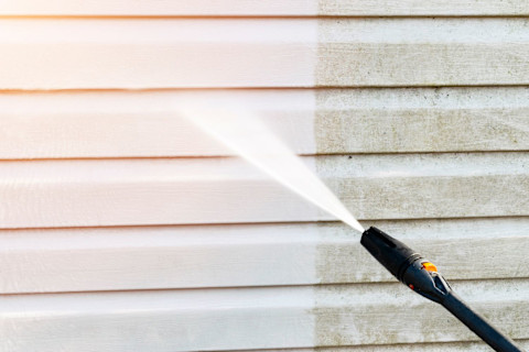 Gevelreiniging met een hogedrukreiniger, een schoonmaker spuit water tegen de gevel om vuil en aanslag te verwijderen.