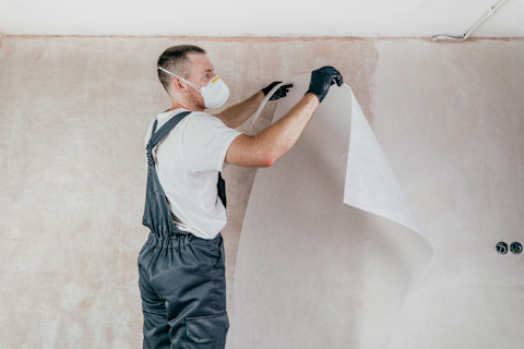 Behanger in overal met handschoenen en beschermend gezichtsmasker is bezig met het aanbrengen van renovlies behang op de muren
