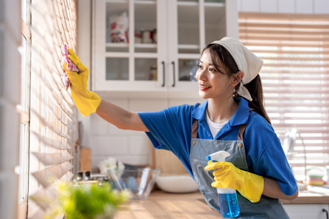 Een professionele schoonmaakster in uniform die een huis schoonmaakt met moderne apparatuur.
