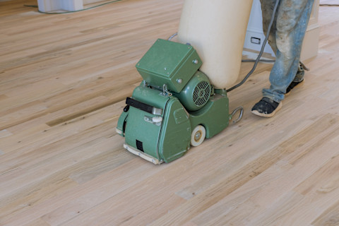 Een groene machine maakt een parket vloer schoon door hem te schuren
