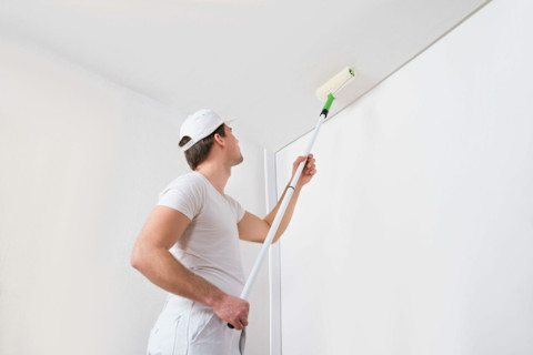 Man schildert een wit plafond met een verfroller op een uitschuifbare steel, close-up van het schilderproces.