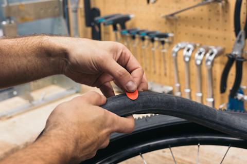 Fietsenmaker plakt een lekke band met een rode plakker, close-up van handen tijdens reparatie.