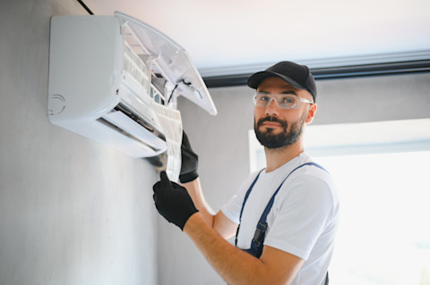 Monteur repareert airconditioningsysteem aan buitenunit van een split airco aan een woningmuur.