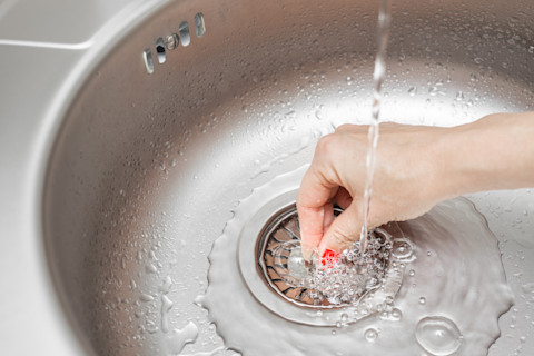 Vrouw sluit de afvoer van de gootsteen af met een rubberen stop om water in de wasbak te houden.
