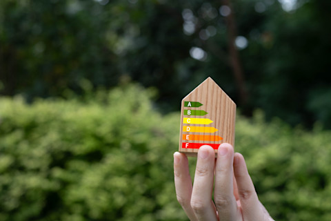 Hand houdt een houten huisje vast met energie-iconen die verduurzaming en energiebesparing symboliseren