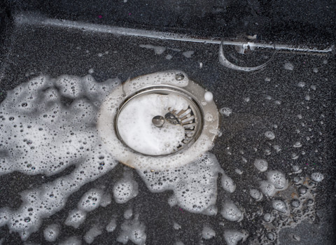 Schuimend water stroomt in een afvoerputje, duidelijk teken van ophoping of verstopping.