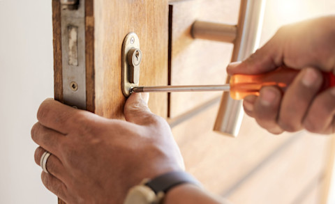 Slotenmaker vervangt een deurslot met gereedschap, close-up van handen en cilinderslot.