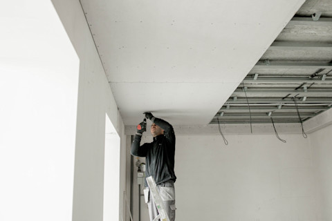Werknemer bevestigt gipsplaat op metalen frame voor verlaagd plafondconstructie.
