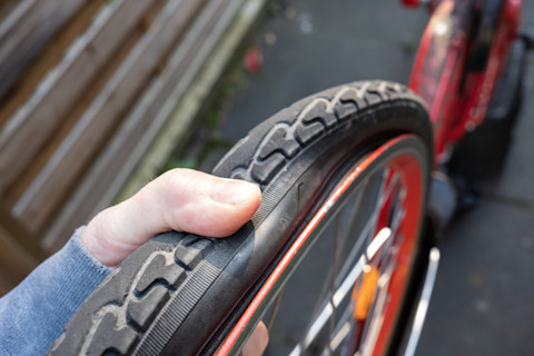 Vinger drukt op een lekke fietsband om het zachte en doorluchtte gedeelte te controleren.