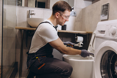 Een vakman zit voor een toilet in een badkamer, hij repareert deze.