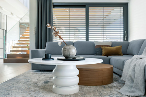 Hoek van een woonkamer met houten jaloezieën, een rotan stoel en natuurlijke raamdecoratie in moderne stijl.