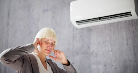 Vrouw houdt haar oren dicht vanwege het harde geluid van de airconditioner dat hoofdpijn en stress kan veroorzaken