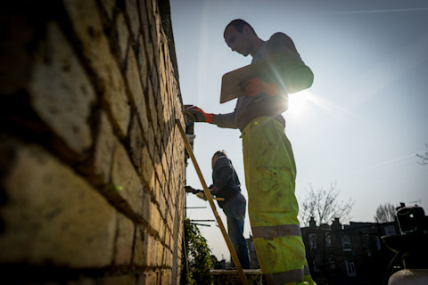 Een vakman werkt aan de voegen van een buitenmuur met bakstenen