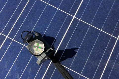 Kompas dat op een zonnepaneel ligt als symbool voor het belang van de juiste oriëntatie.