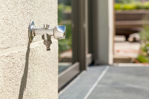 Buitenkraan gemonteerd op een buitenmuur met stromend water.