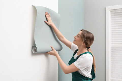 Vrouw verwijdert behang van een muur, zichtbaar halverwege het losmaken van de stroken.