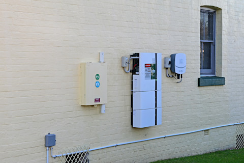 Thuisbatterij en omvormer voor zonne-energie geïnstalleerd aan de zijkant van een woning.