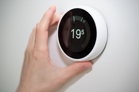 Iemand stelt een slimme thermostaat in, als voorbeeld van slimme warmte- en energiecontrole