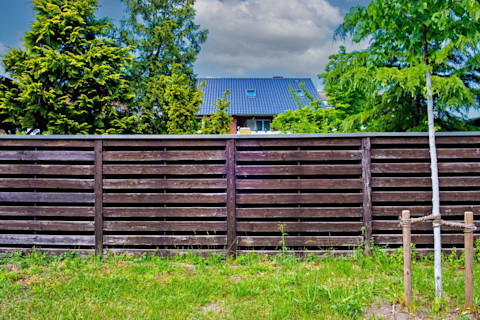 Een donkerbruine schutting in een groene tuin