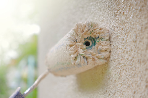 Verfroller met beige verf op houten oppervlak tijdens buitenschilderwerk in detail weergegeven.