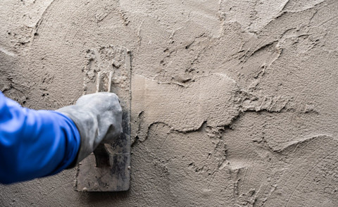 Hand van stukadoor brengt pleister aan op een cementmuur.