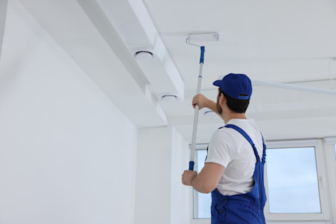 Binnenschilderwerk van het plafond met een roller door een schilder in blauw overal.