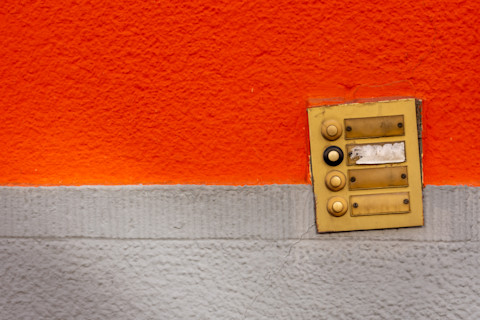 Een oude, kapotte deurbel bevestigd aan een verweerde muur, met zichtbare beschadigingen en roest, wat duidt op slijtage en de noodzaak van vervanging.  