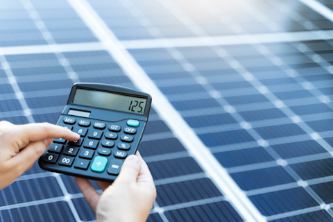 Zonnepanelen naast een rekenmachine, illustrerend hoe je met duurzame energie geld kunt besparen.