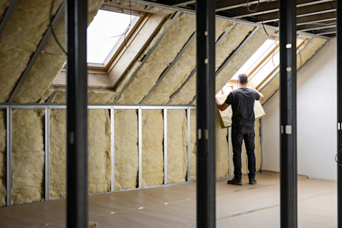 Man plaatst isolatiepanelen in een schuin dak tijdens werkzaamheden aan woningisolatie