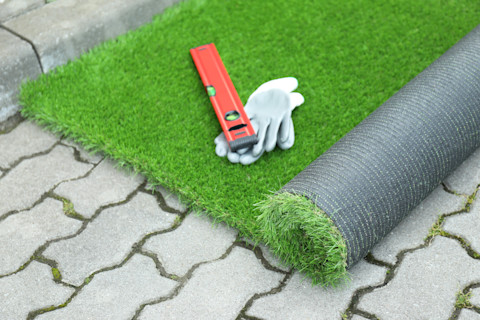 Werkhandschoenen, waterpas en rol kunstgras liggen klaar op een bouwplaats voor installatie.