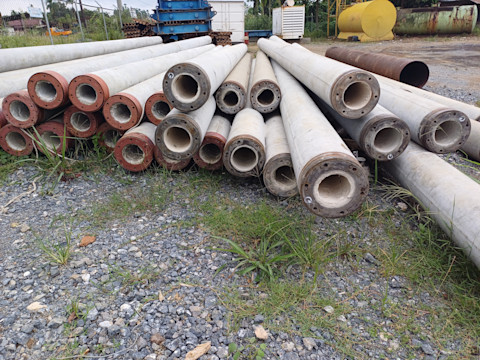 Een stapel grote betonnen heipalen ligt op een onverhard terrein, klaar voor gebruik op een bouwplaats.