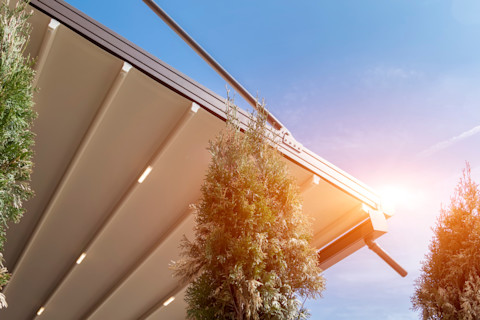 Zonwering van canvas gespannen over metalen frame met zicht op waterafvoerbuis, bescherming tegen directe zon.