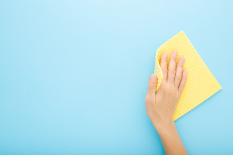 Vrouwelijke hand houdt een gele spons tegen een witte muur met zichtbare vlekken.