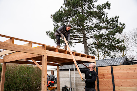 Twee mannen die markiezen van hout plaatsen in een tuin.