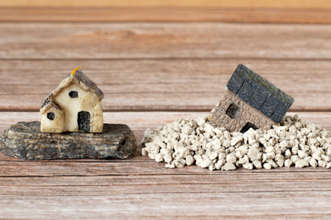 Twee miniatuurhuizen geplaatst op zand en een stevige rots.
