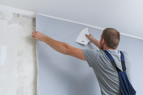 Man plakt grijs vinylbehang op een muur tijdens renovatie.