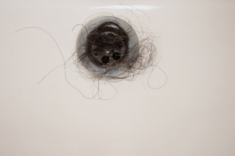 Gootsteen verstopt met donkere haren, duidelijk zichtbaar in de afvoer.