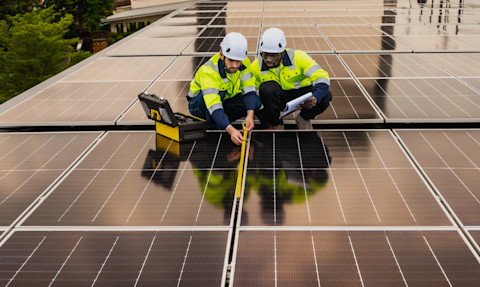 Twee monteurs installeren zonnepanelen op een schuin dak.