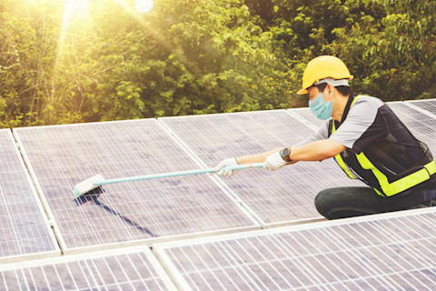 man met masker reinigt zonnepanelen op een dak met schoonmaakmiddelen.