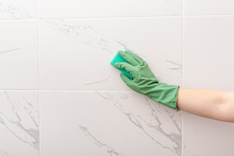  Een hand met handschoen maakt met een spons een badkamer muur schoon