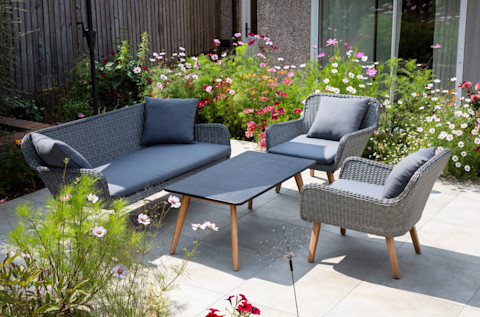 Tuinmeubels op een zonnig terras met houten vlonder en groene omgeving.