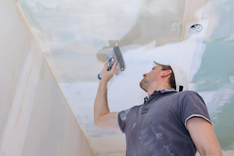 Bouwvakker kijkt omhoog naar net gestuct plafond in woning.