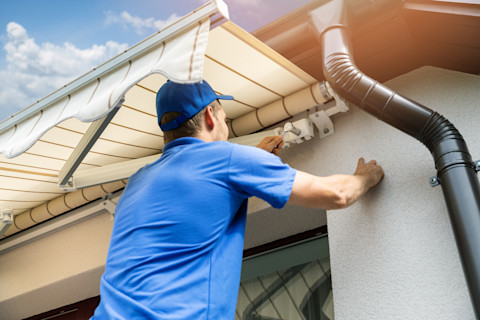 Een monteur bevestigt een zonnescherm aan de gevel van een woning. Hij werkt met gereedschap voor montage.