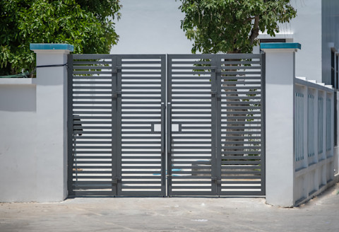 Elektrische poort bij een moderne woning, met aparte doorgangen voor voetgangers en auto's.
