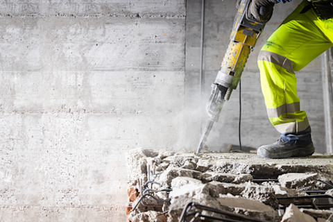 Vloerspecialist gebruikt een drilboor om een betonnen vloer buiten in een tuin te slopen