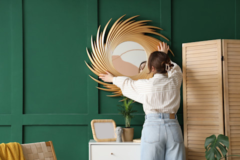 Jonge vrouw hangt een gouden spiegel op een witte muur in haar interieur