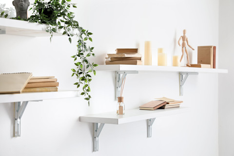 Een aantal witte planken op een muur met decoratieve elementen zoals kaarsjes en planten