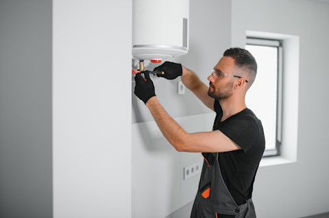 Een vakman onder een boiler controleert leidingen en aansluitingen tijdens servicewerkzaamheden.