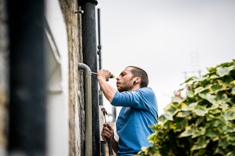 Loodgieter werkt aan de regenpijp aan de buitenkant van een woning
