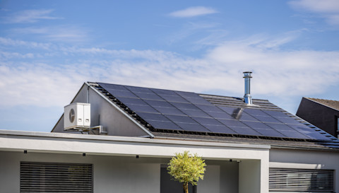 Zonnepanelen op het dak van een modern huis met een airco buitenunit zichtbaar.